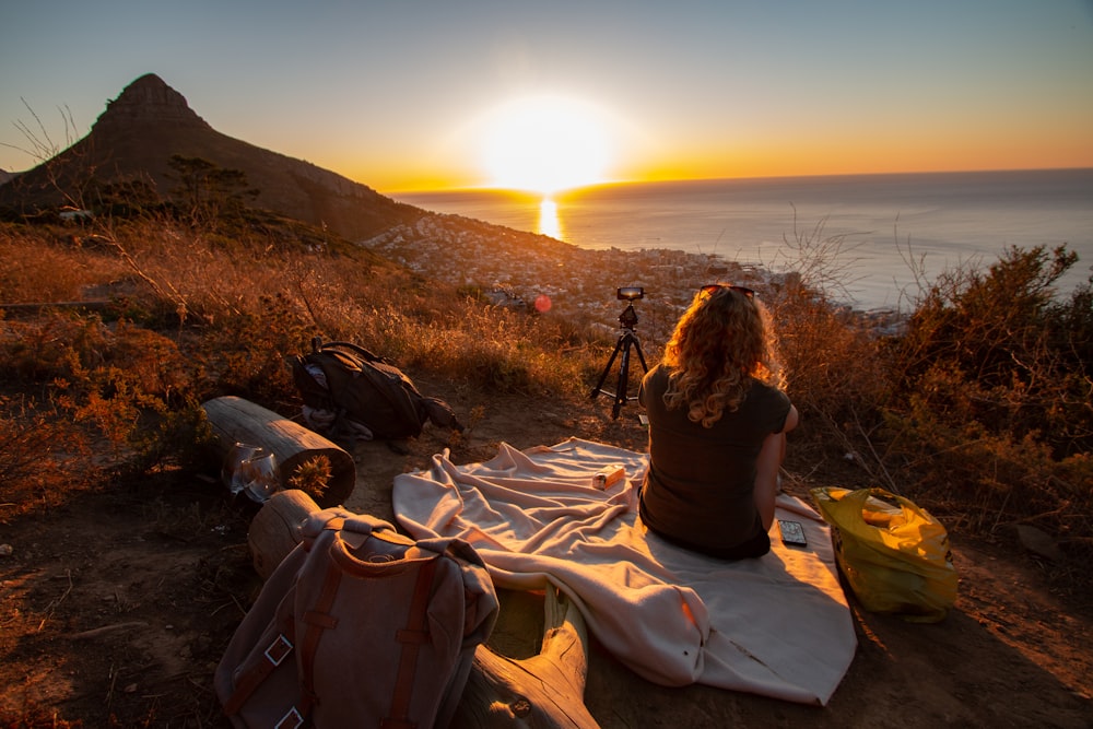 woman sitting on blanket near sea and mountain during dawn